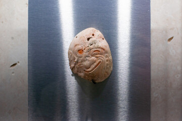 smiling winking asymmetrical face carved from limestone on a brushed stainless steel plate