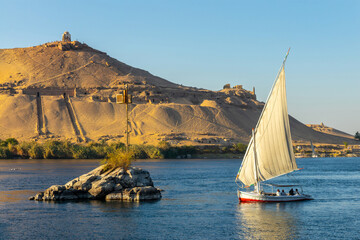 Felucca (traditinal egyptian sailing boat) on the Nile river and the Dome of Abu Al-Hawa (Qubbet el-Hawa) or Dome of the Wind in Aswan, Egypt - obrazy, fototapety, plakaty