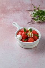 Fruit salad with watermelon balls and mozzarella cheese in white ceramic bowl on light rose background