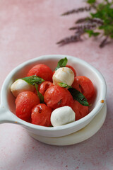 Watermelon Salad with mozzarella balls and mint on light rose background. healthy eating. Summer recipe concept