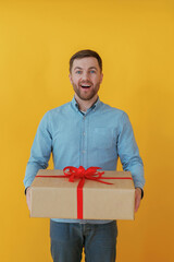 Surprised, holding gift box. Attractive man in blue shirt is against yellow background