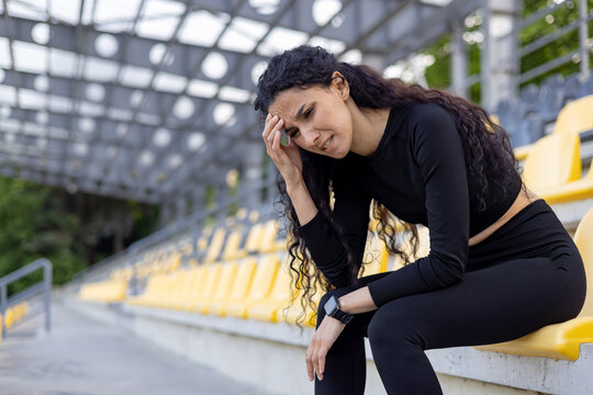 An athletic woman in sportswear taking a rest on yellow stadium seats after exercising. Concept of fitness and healthy lifestyle.