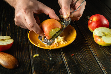 Preparing a dietary dish with apples. Chef grates a raw apple with a grater on the kitchen table. Advertising space on a black background