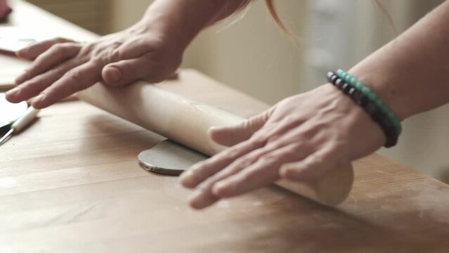 Woman in apron rolling clay on wooden table for making pottery on ceramics masterclass
