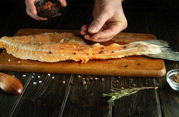 Cooking fish at home. Man hands add spices to fish steak on vintage kitchen table.