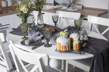 Easter festive spring table setting decoration, eggs in nest, fresh yellow tulips in vase, marshmallows, feathers, family dinner or breakfast concept, toned