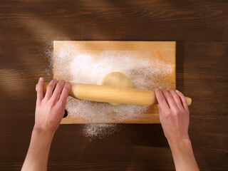 Rolling out the dough in flour on wooden board.