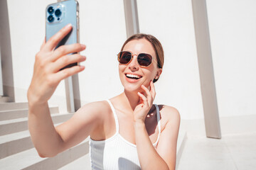 Beautiful smiling model in sunglasses. Female dressed in summer hipster white T-shirt and jeans....