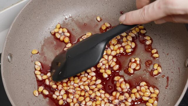 Corn kernels for popcorn are fried in red sugar syrup and stirred.