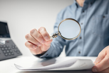 Man with magnifying glass reading documents or legal contract - 764803210