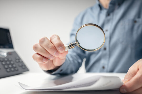 Man with magnifying glass reading documents or legal contract