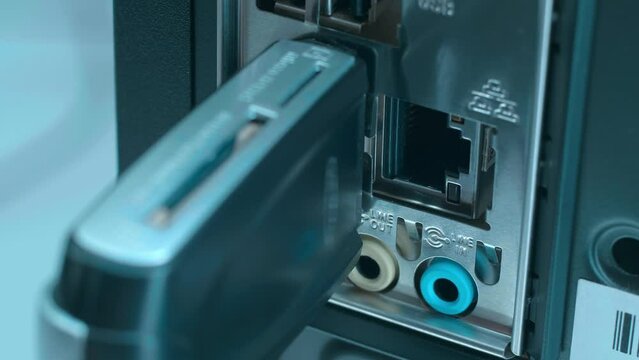 A man's hand inserts and removes a SD card reader into the USB port on the back panel of the computer. Closeup. Macro