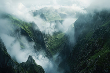 Cinematic shot of the view from above, looking down at an epic mountain range with clouds rolling over and mist hanging in between mountains, green grass on cliffs - obrazy, fototapety, plakaty