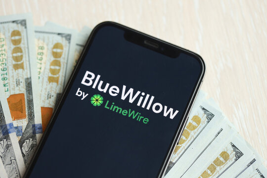 KYIV, UKRAINE - MARCH 17, 2024 BlueWillow logo on iPhone display screen with many hundred dollar bills. Artificial Intelligence engine