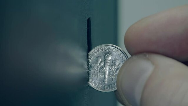 Male fingers inserting a 10 cent coin into a coin receiver, the light is brightly reflected from the surface of the coin. Closeup. Macro