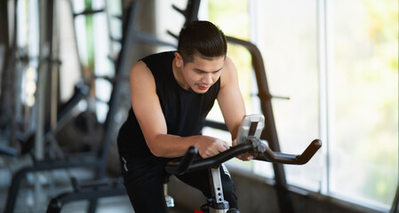 Asian sportsman exercising on a bicycle in the gym, determination to cardio lose weight, makes her healthy. exercise bike man fitness sport concept.