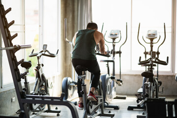 Back view. Asian sportsman exercising on a bicycle in the gym, determination to cardio lose weight,...