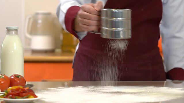 Flour on table. Man's hands sift flour. Preparing ingredients for baking dough, pasta. Making bread, workplace, professional kitchen interior. Cook's hand sift flour through sieve. 