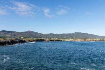 A serene coastal landscape with clear skies, calm waters, and distant green hills offering a...