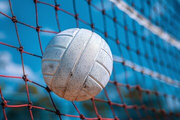 Vibrant outdoor photograph depicting a textured white volleyball ensnared in a red sports net...