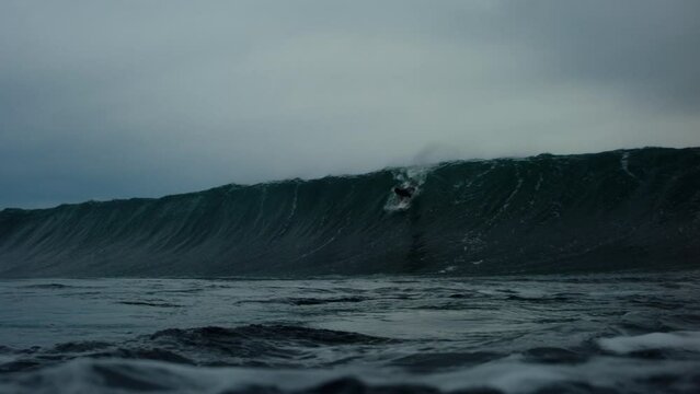 Low angle in water POV of surfer dropping in on steep winter wave leaning back to pull into barrel