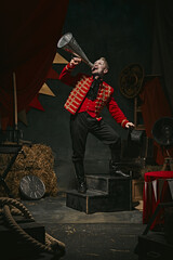 Announcement. Poster. Ringmaster, magician in red coat shouting into megaphone over dark retro circus backstage background. Concept of circus, theater, performance, show, retro and vintage