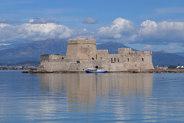 Fototapeta na wymiar Beautiful small castle of Bourtzi built at sea a popular attraction in city of Nafplio former capital of Greece as seen at spring morning with nice white clouds and deep blue sky, Argolida, Greece