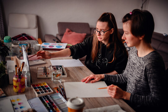 Two women engage in an artistic collaboration, they drawing together in a cozy creative space