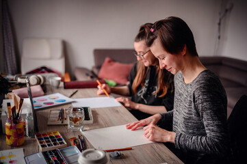 Two women engage in an artistic collaboration, they drawing together in a cozy creative space