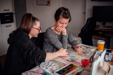 Two artists share a moment of creation, painting with watercolors in a home setting, showcasing teamwork and artistic expression