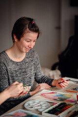 An artist smiles gently while immersed in the flow of watercolor painting, surrounded by art...