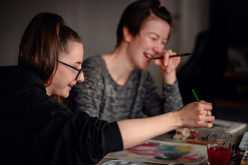 Two friends share laughter and joy while engaged in watercolor painting, illustrating the pleasure of artistic hobbies.