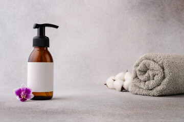 Obraz na płótnie Canvas A minimalist spa setup featuring a brown pump bottle with a blank label, accompanied by a delicate purple orchid flower and soft white cotton towel in the background