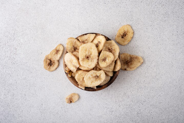 Fototapeta na wymiar Dried sliced bananas placed in a wooden bowl and scattered around on a textured grey surface