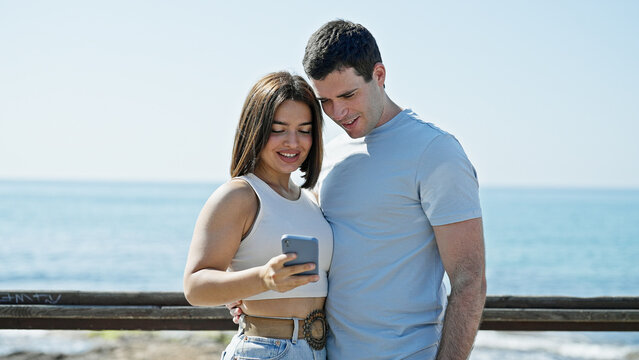 Beautiful couple smiling confident using smartphone at seaside