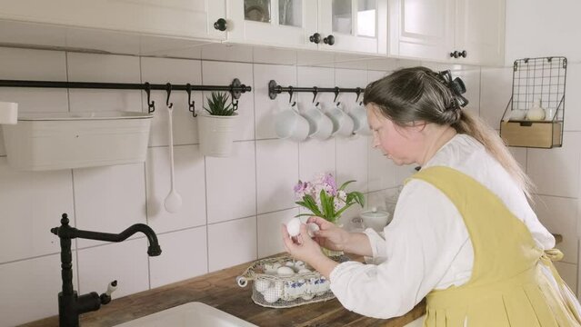 mature woman in yellow apron preparing Farm-fresh chicken eggs in kitchen, Easter egg dyeing celebration, Cooking traditions, Domestic rituals, Dietary choices, Kitchen activities