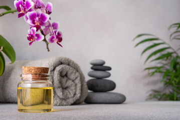 A serene spa still life featuring essential oils, smooth pebbles, a rolled grey towel, and a...