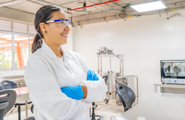 mujer joven con sus manos cruzadas sonriendo y usando proteccion mientras trabaja en un laboratorio...