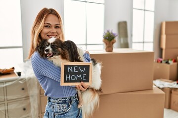 Young caucasian woman holding blackboard hugging dog at new home