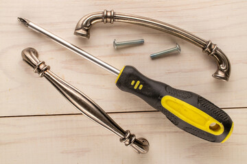Two metal drawer handles, a screwdriver and two screws on a wooden table, top view.