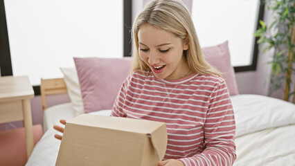 Excited young woman in bedroom opening a parcel, expressing joy and anticipation over new purchase...