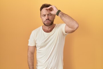 Fototapeta na wymiar Middle age man with beard standing over yellow background worried and stressed about a problem with hand on forehead, nervous and anxious for crisis