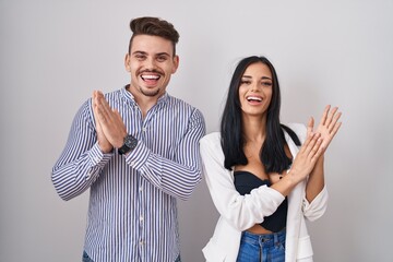 Young hispanic couple standing over white background clapping and applauding happy and joyful,...