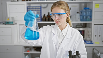 Fototapeta premium Blonde woman scientist examining a blue liquid in a flask in a laboratory setting
