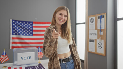 Blonde woman pointing at camera in a usa voting center with american flags