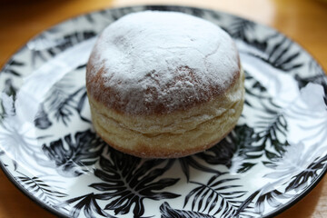 Donut with icing sugar on a plate on a wooden table.