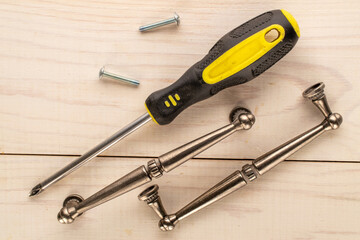 Two metal drawer handles, a screwdriver and two screws on a wooden table, top view.