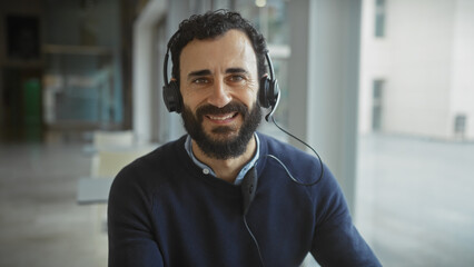 Handsome middle-aged man with beard and headphones smiling in a modern office setting