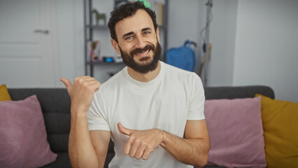 Bearded man pointing sideways with thumbs in a living room