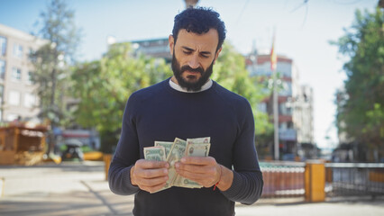 A mature, bearded man counts money outdoors on a sunny city street, portraying everyday financial...